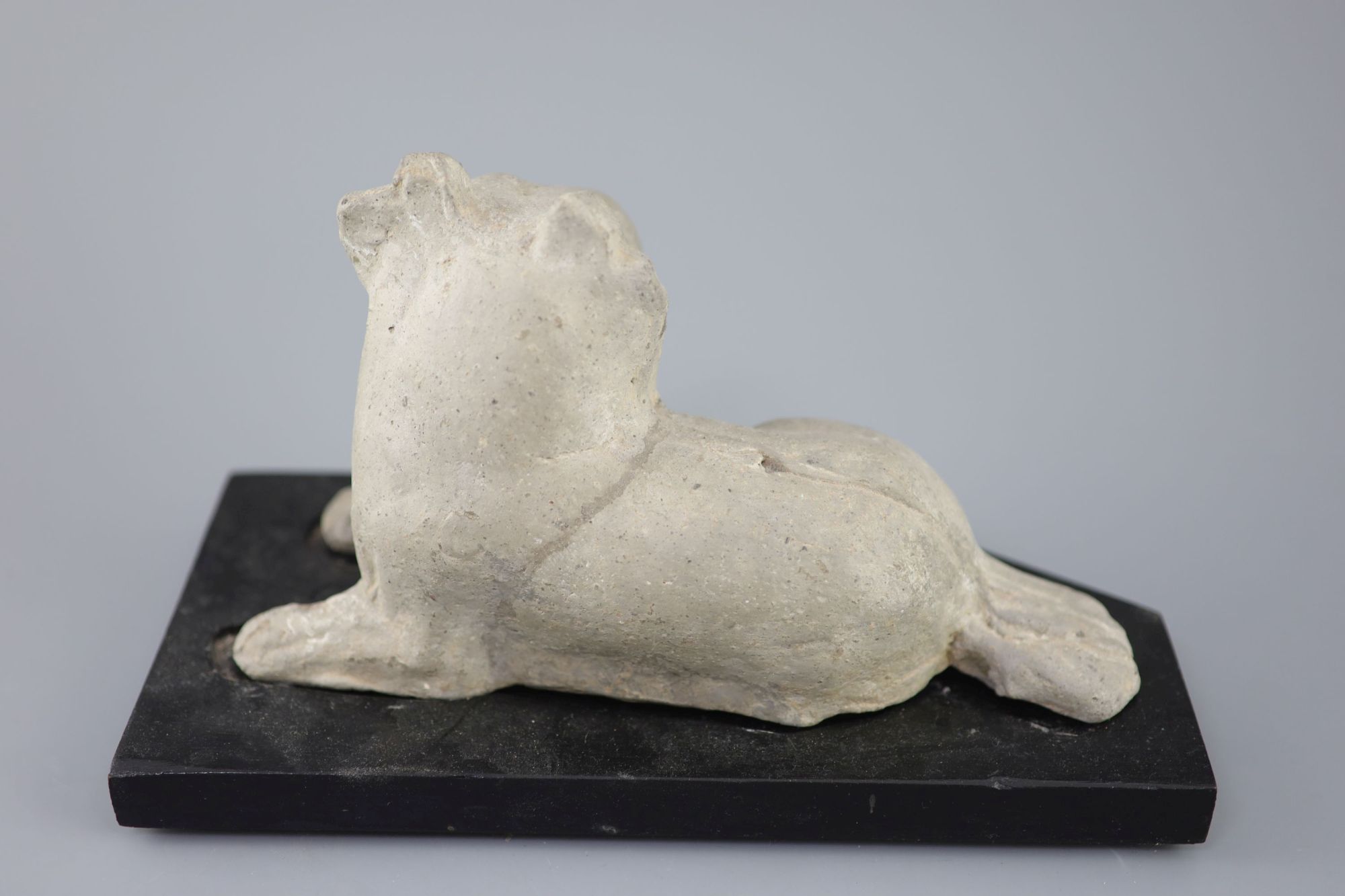 A Chinese grey pottery figure of a recumbent dog, Han dynasty or later 23.5cm long, wood stand